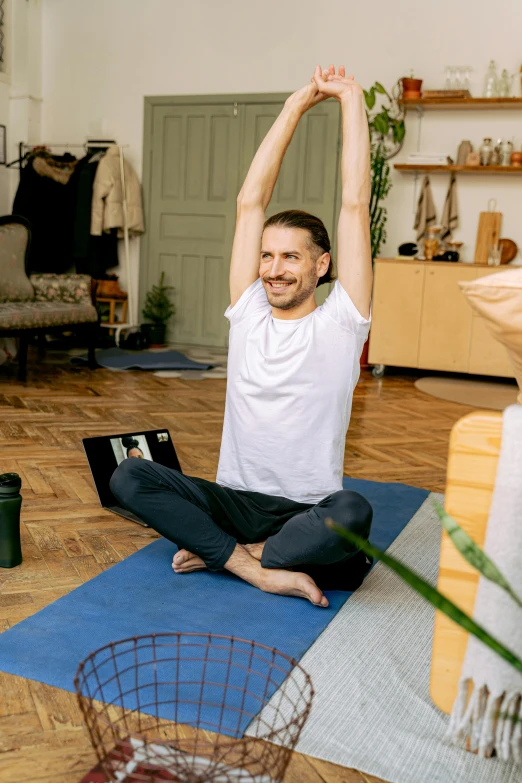 man sitting on the floor in front of laptop doing yoga