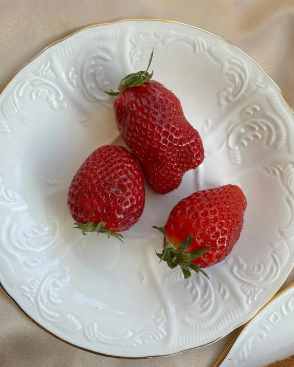 three strawberries are placed on a white plate