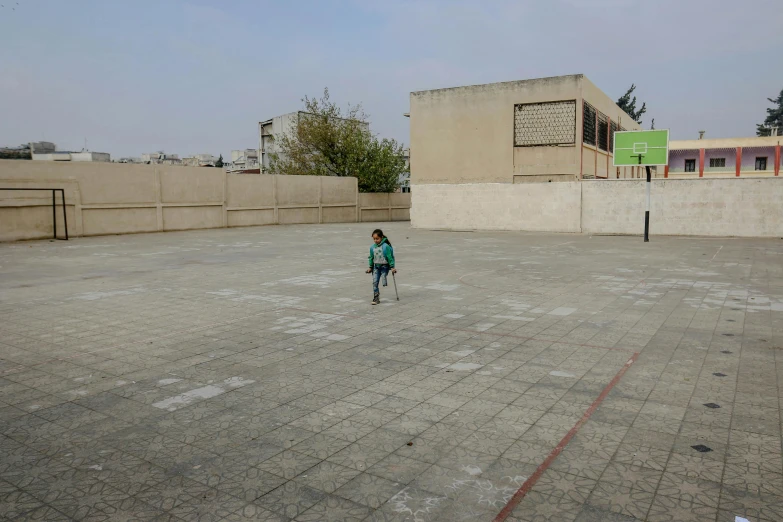 a girl walking across an empty courtyard with buildings in the background