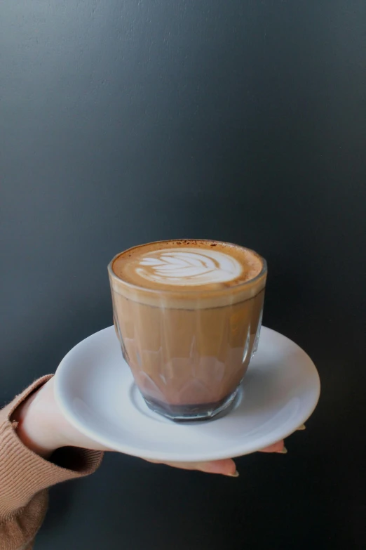 a person holding a white saucer with a cup of liquid in it