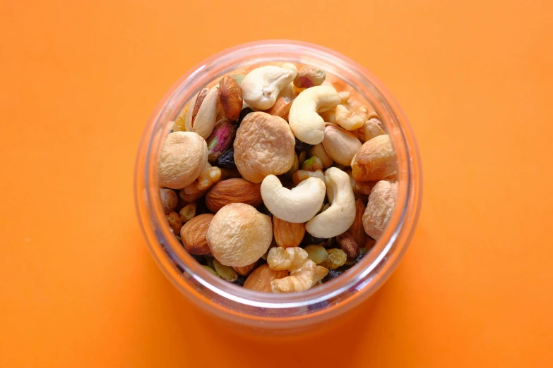 a jar filled with mixed nuts on top of an orange background