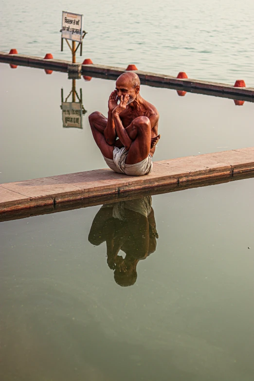 a man sitting in the water next to a railing with his reflection on the water
