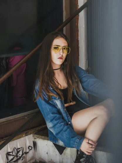 woman in yellow sunglasses, blue jean jacket and skirt sitting on a wall