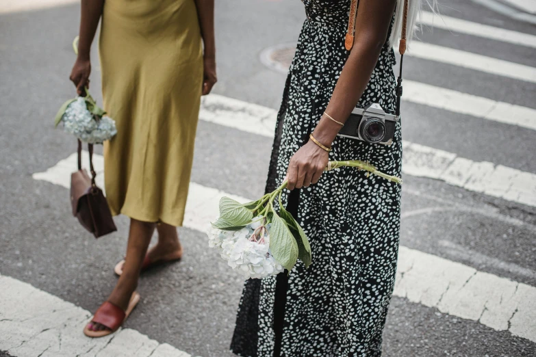 two women cross a street at an intersection holding bouquets