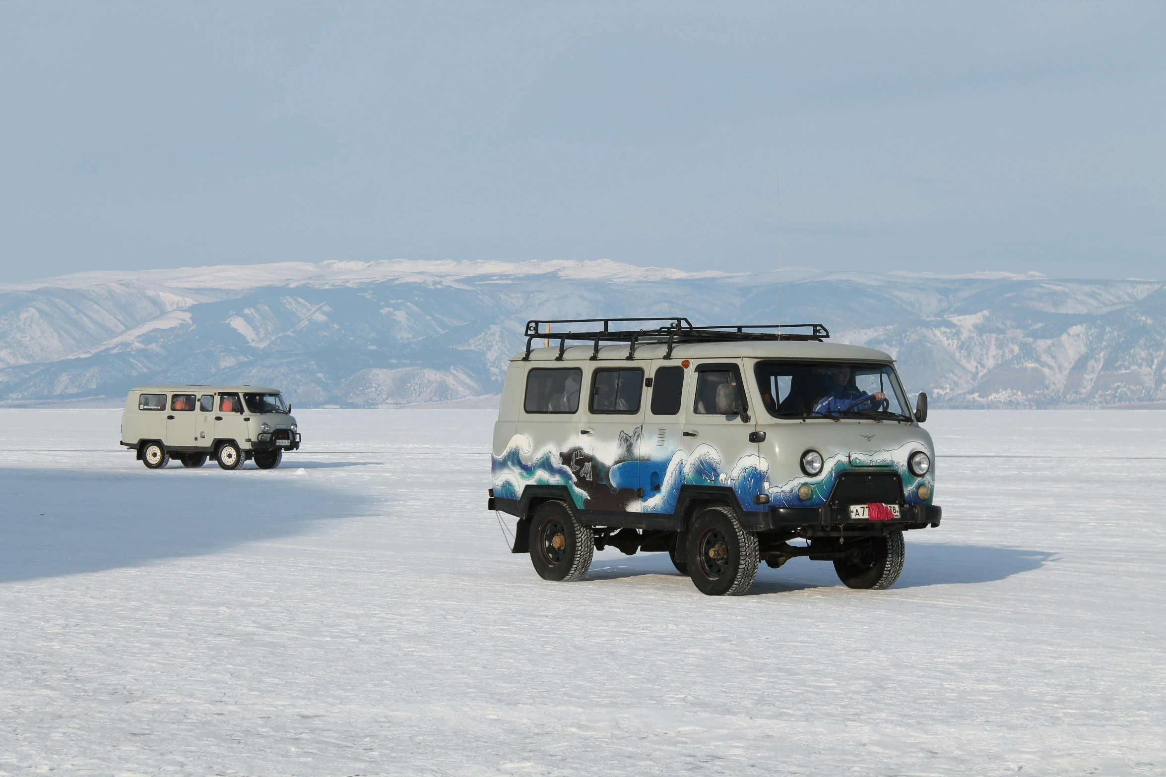 two white vehicles on a snowy surface with mountains in the background