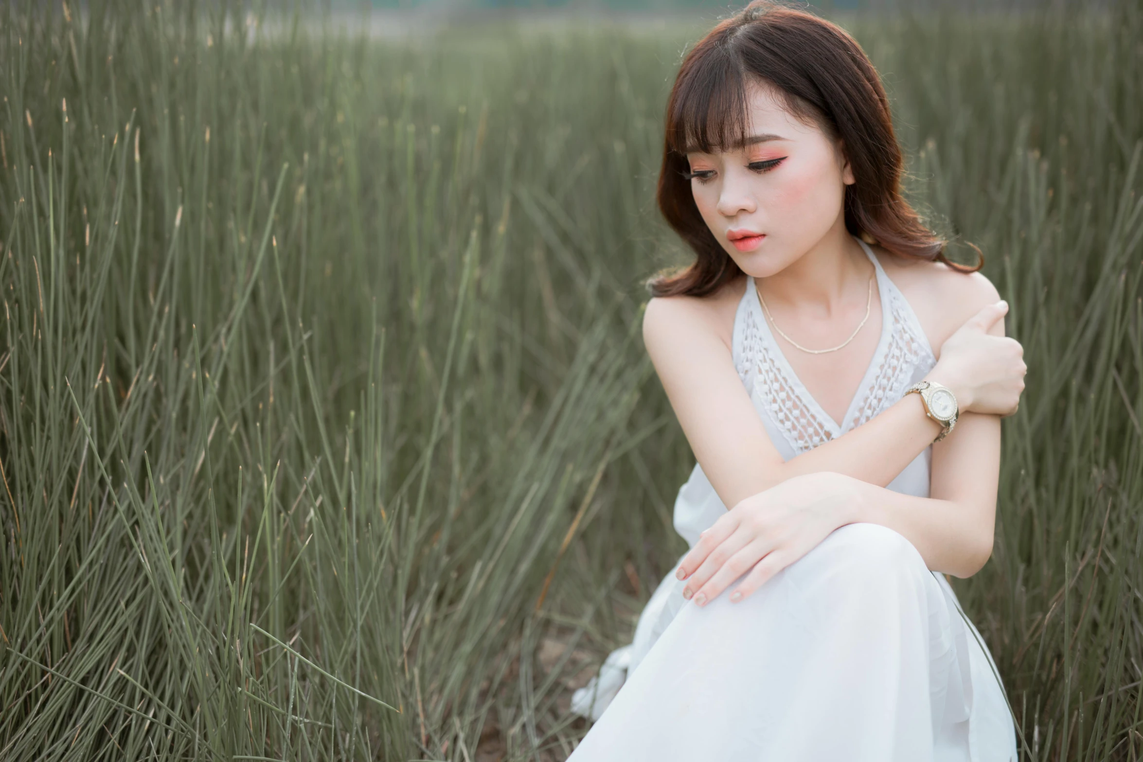 a woman in white sits in some tall grass