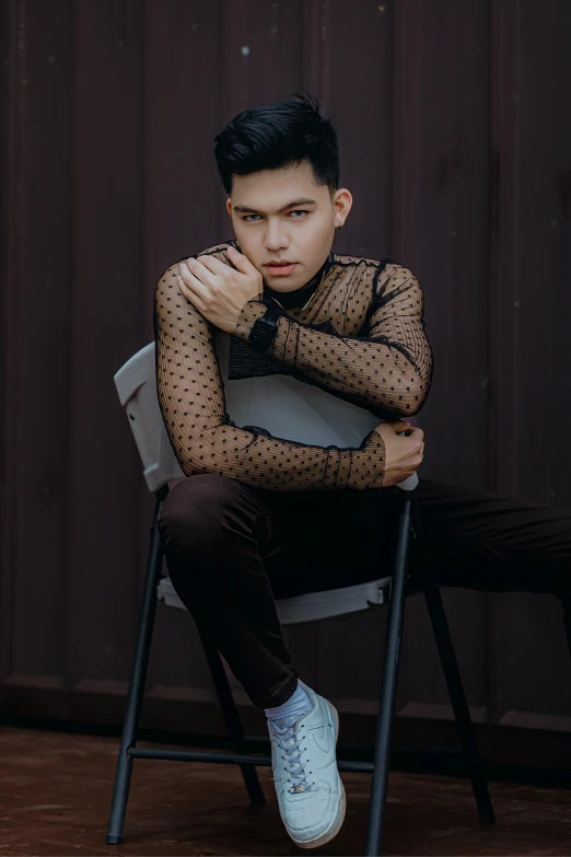 an asian man in black sheer shirt sitting on a chair