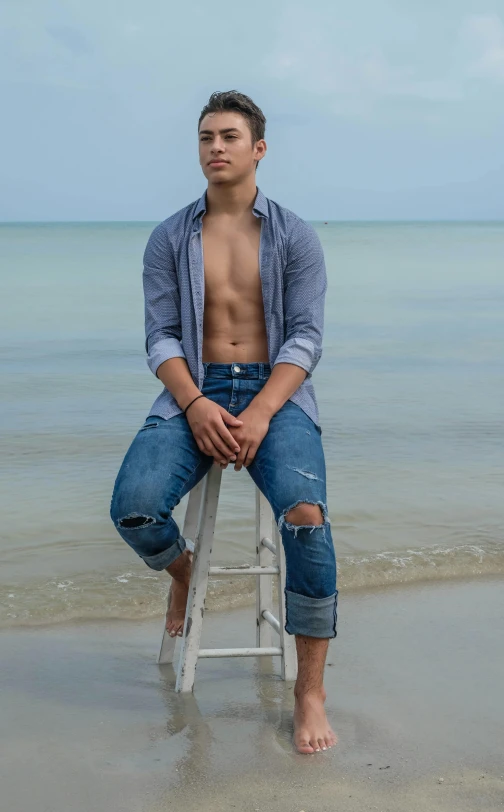 a man sitting on top of a white stool near the ocean