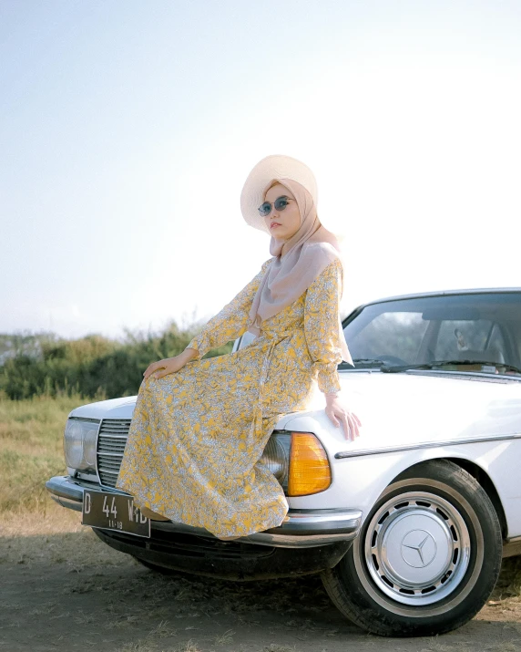 a woman in a floral dress leaning on the hood of a car