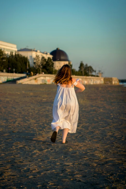 a girl runs across the sand and throws her white frisbee