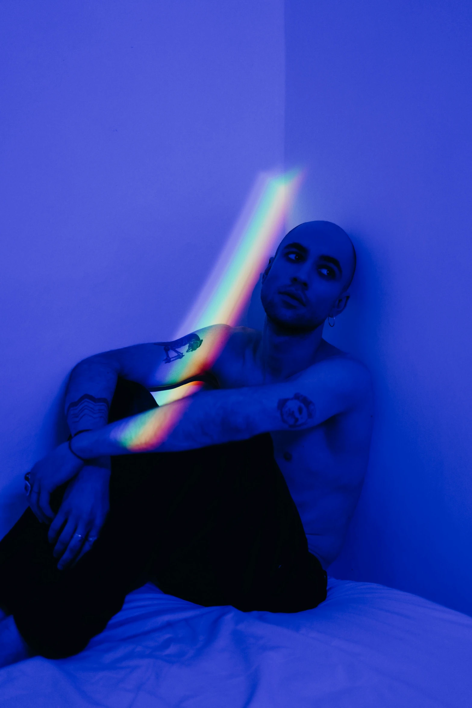 a man sitting on a bed with a rainbow glow painted in the wall