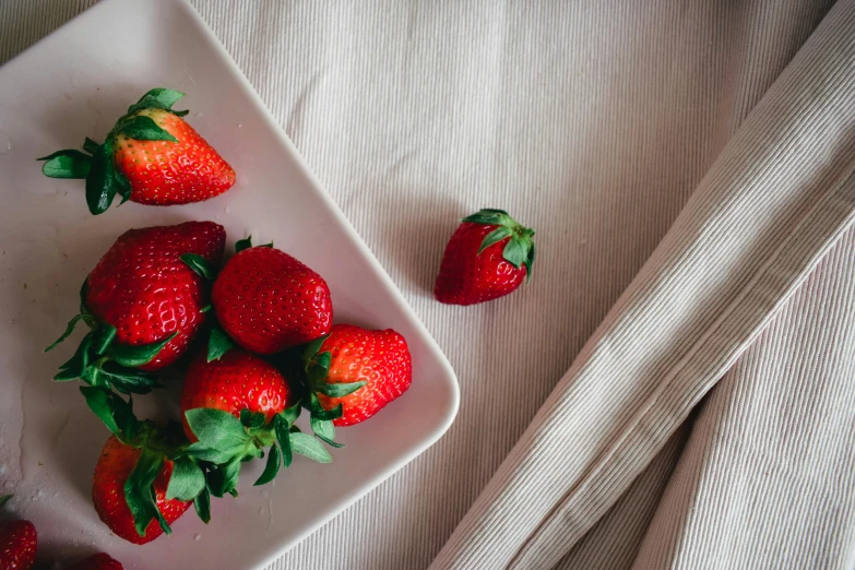 a plate topped with ripe strawberries on top of a white bed