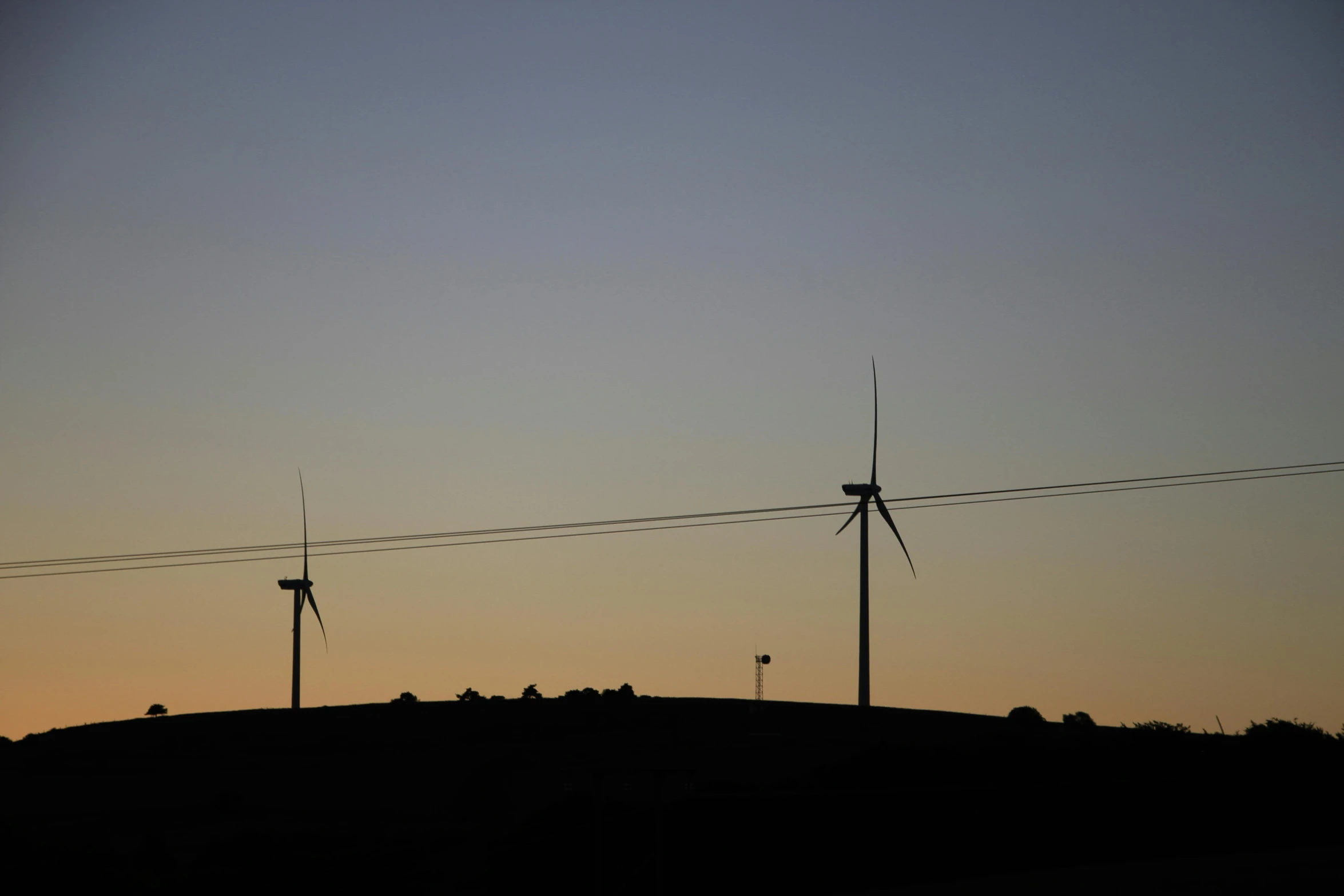 the sun is setting at the top of a hill next to windmills