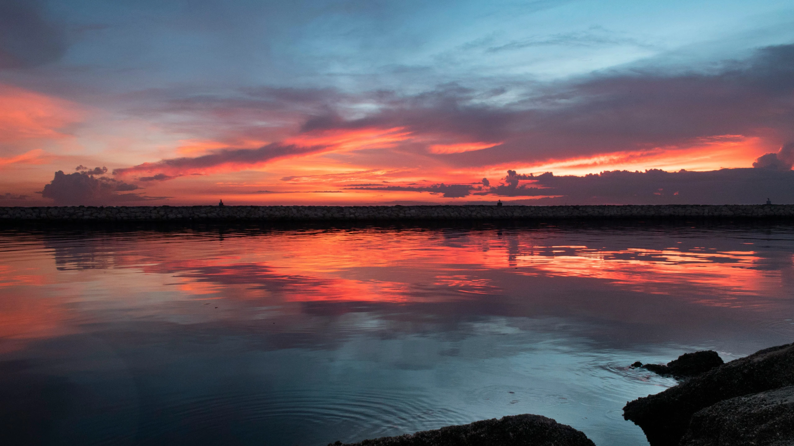 some rocks are on the water and sunset