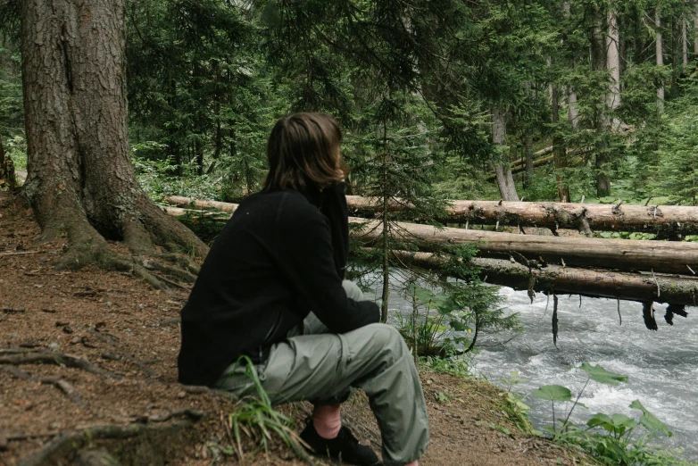 a man sitting on a tree stump in front of a creek