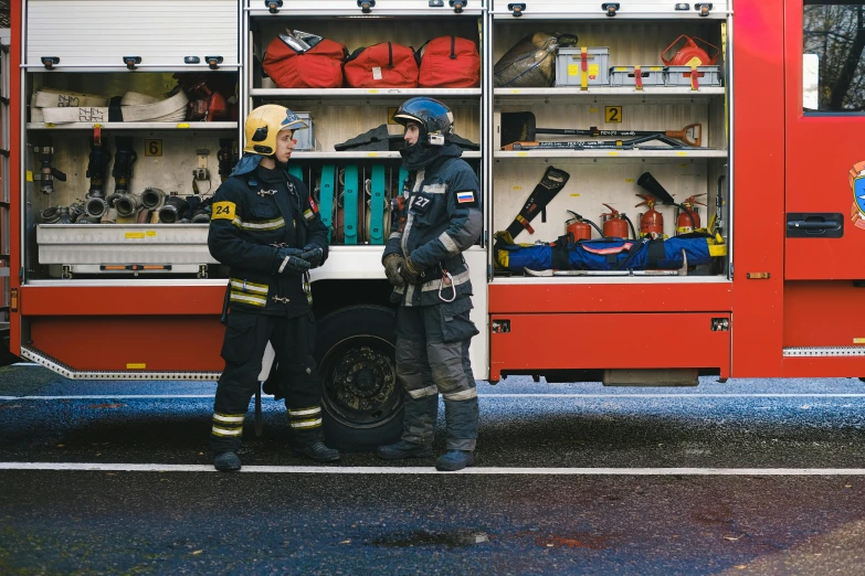 two firemen standing next to a firetruck and the ladder has been broken