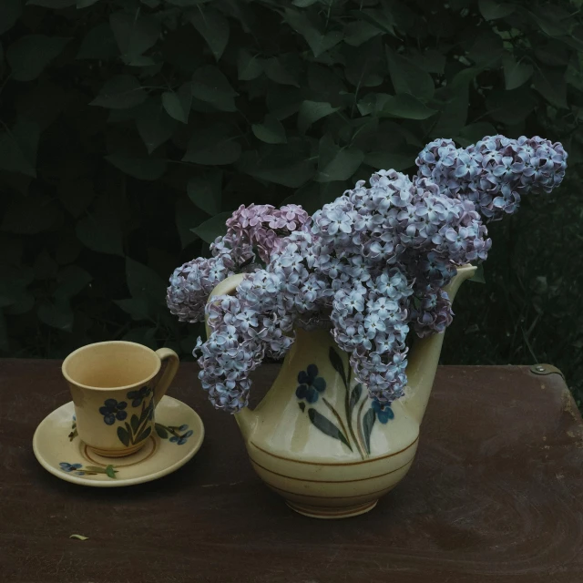 purple and white flowers are in a flower pot and a coffee cup on a table