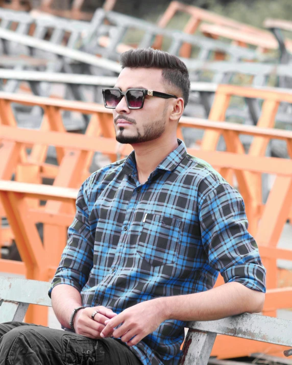 a man wearing a blue plaid shirt sits on a bench