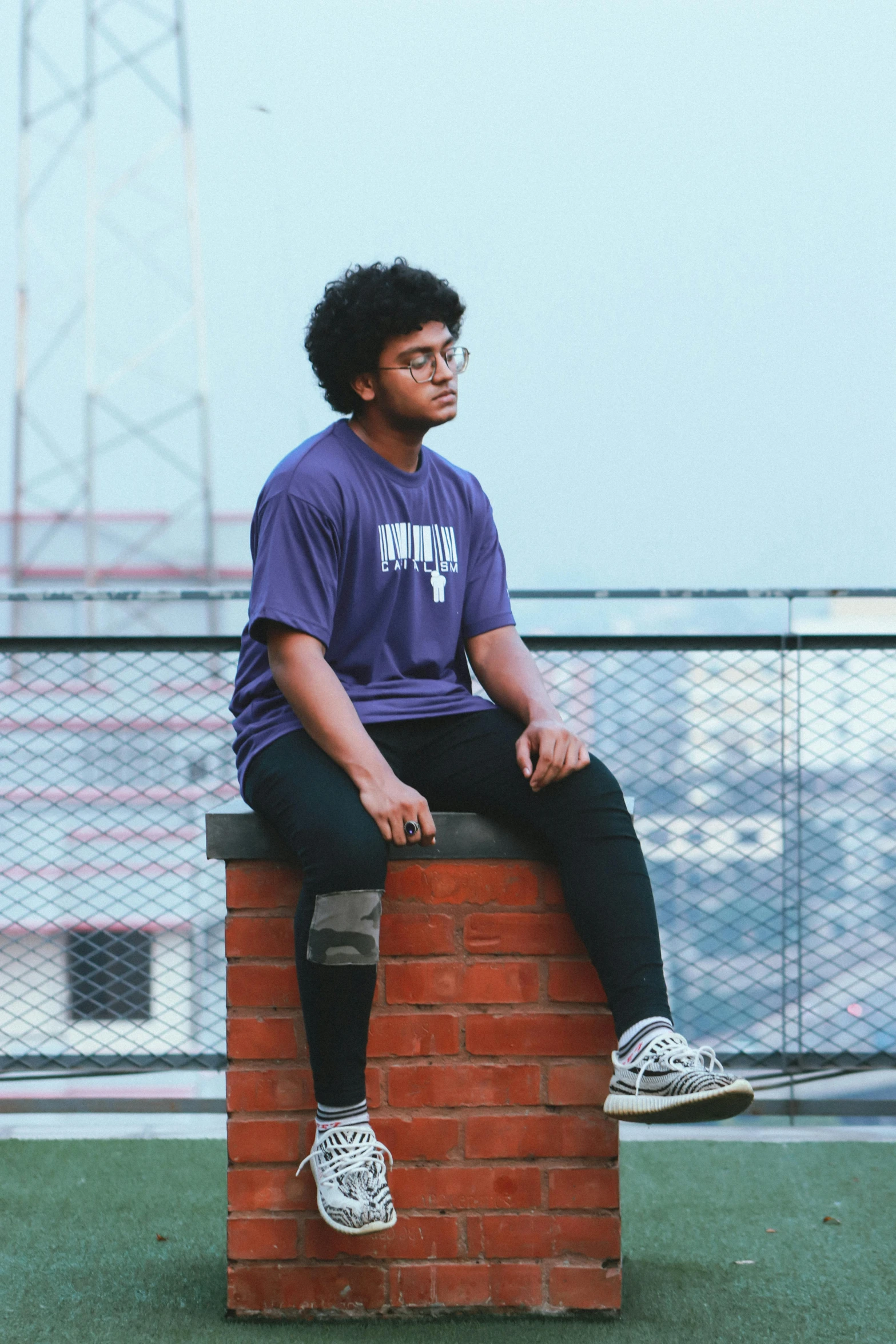 a young man sits on a brick pillar looking off into the distance