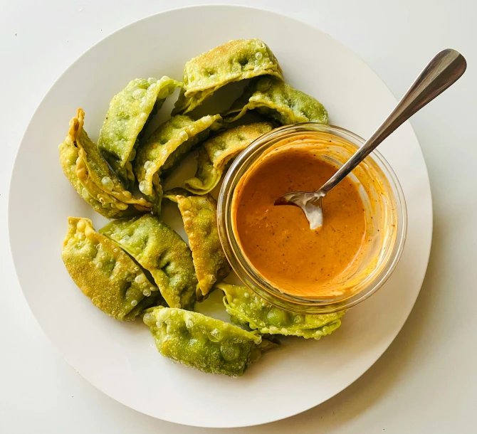 the plate is filled with fried vegetable rings next to a jar of dipping sauce