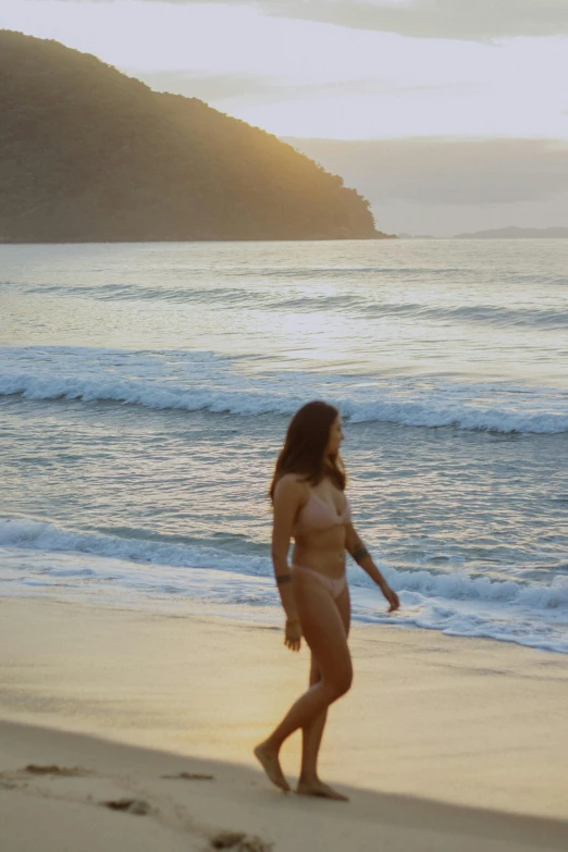 a woman is walking on a beach at dusk