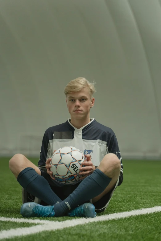 a soccer player sitting on the grass holding a ball