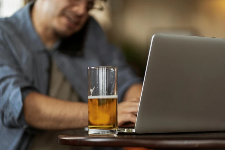 a man is working on his laptop with a beer