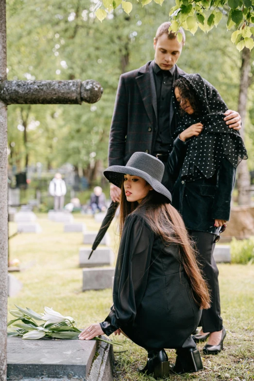 the people are standing around the grave and sitting on a bench