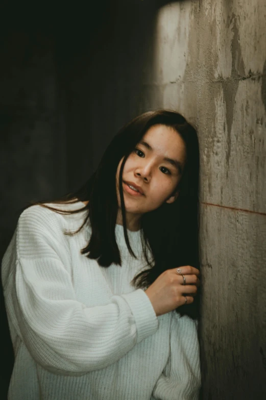 a woman posing against a wall in a white sweater