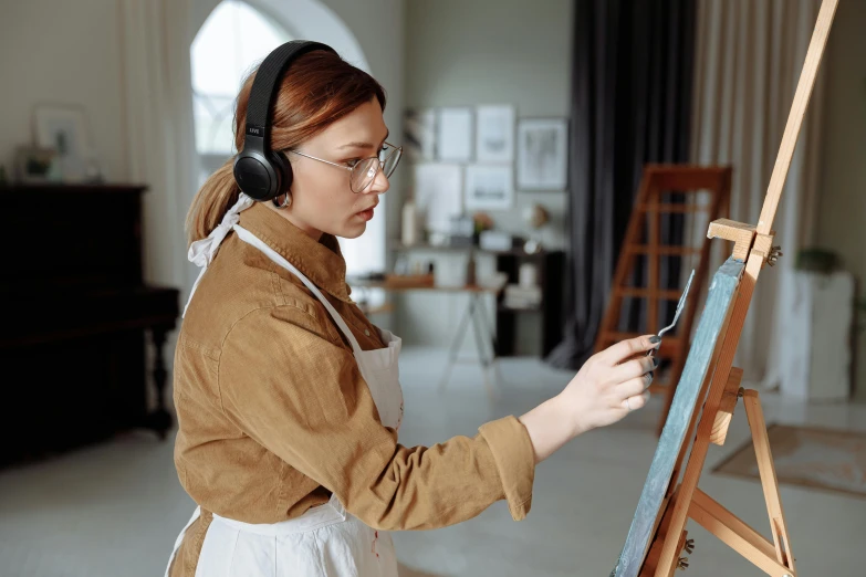 an image of woman painting on easel with headphones