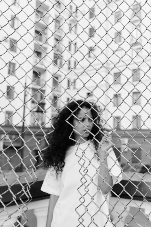 black and white pograph of woman looking through chain link fence