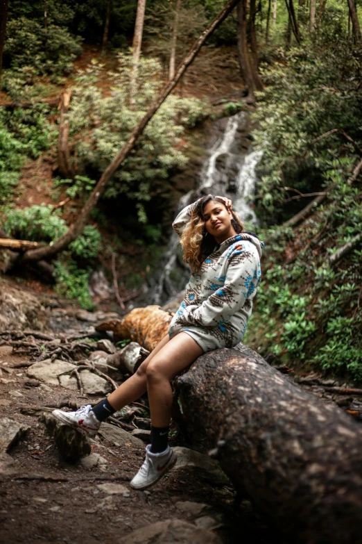 a woman is sitting on a rock next to a waterfall