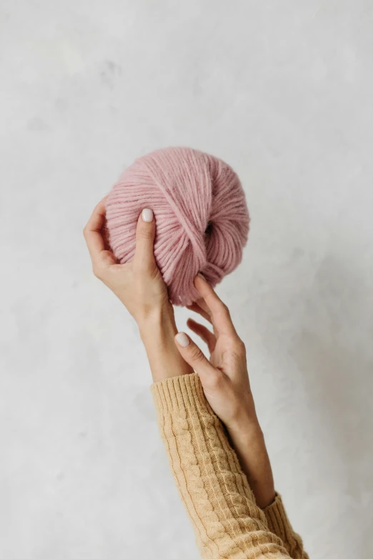 a woman's hand holding up a pink yarn ball