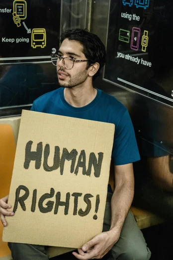 a person sitting on a subway holding up a sign that says human rights