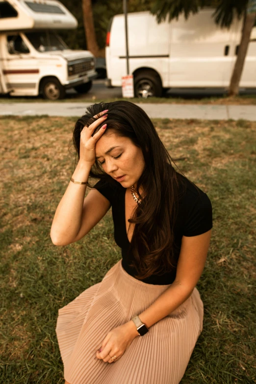 a woman sits in the grass, holding her head with one hand