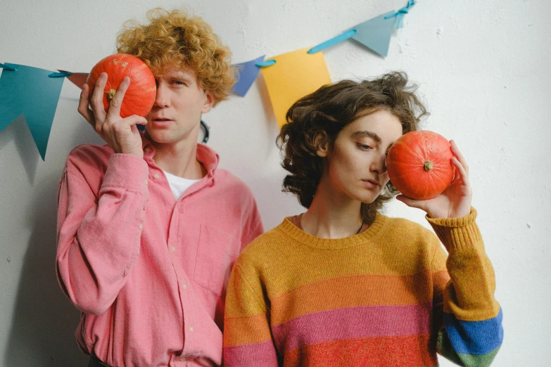 two people in colorful sweaters holding oranges in front of their faces