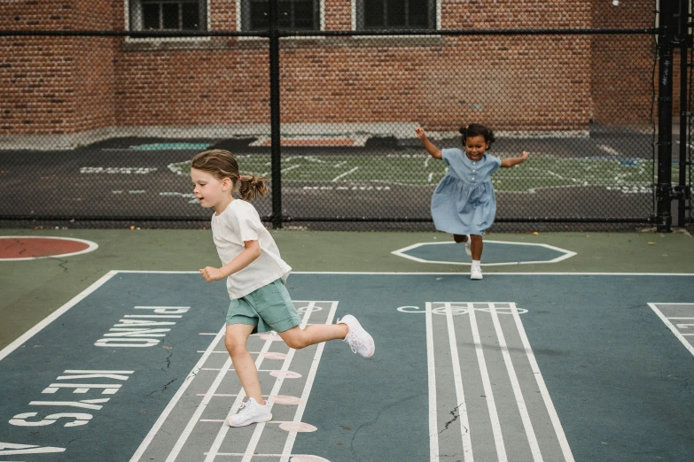 two young children run across a tennis court