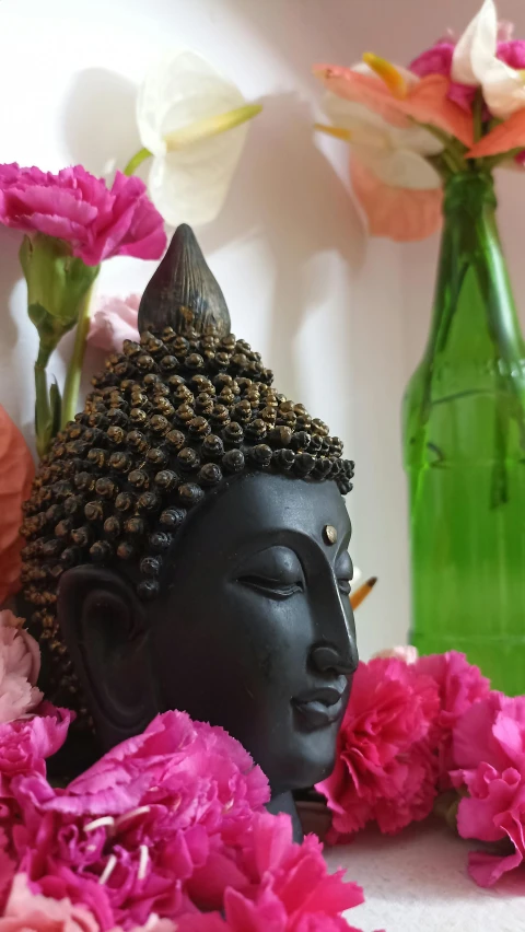 a buddha head with ear spikes sits amongst flower petals in front of two vases