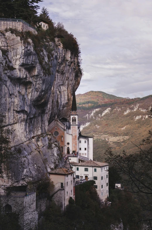 an old style house on a cliff with mountains in the background