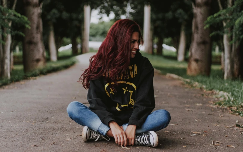 a girl with long red hair and black sweatshirt sitting on a street