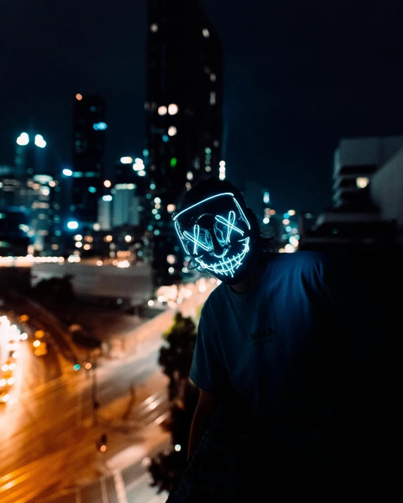 a man wearing a neon mask standing in front of a city