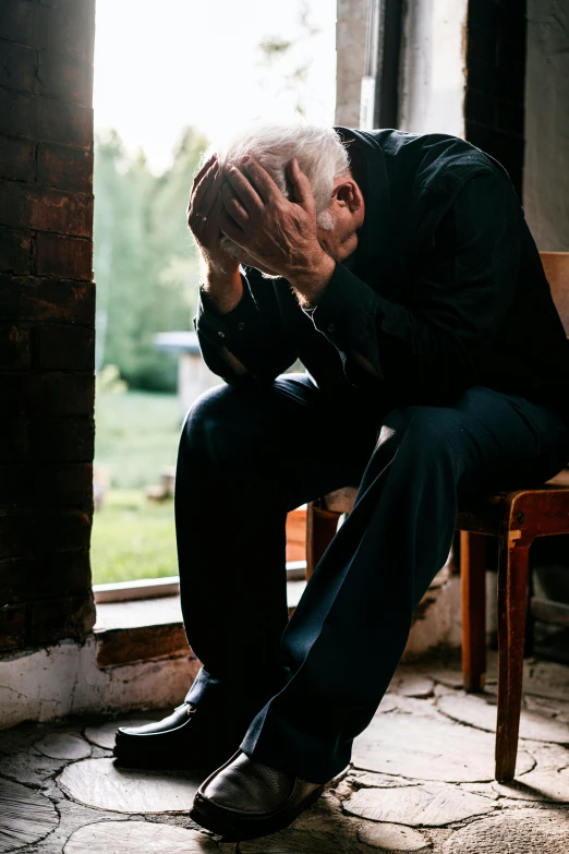 man in black sitting on a brown chair with his head up