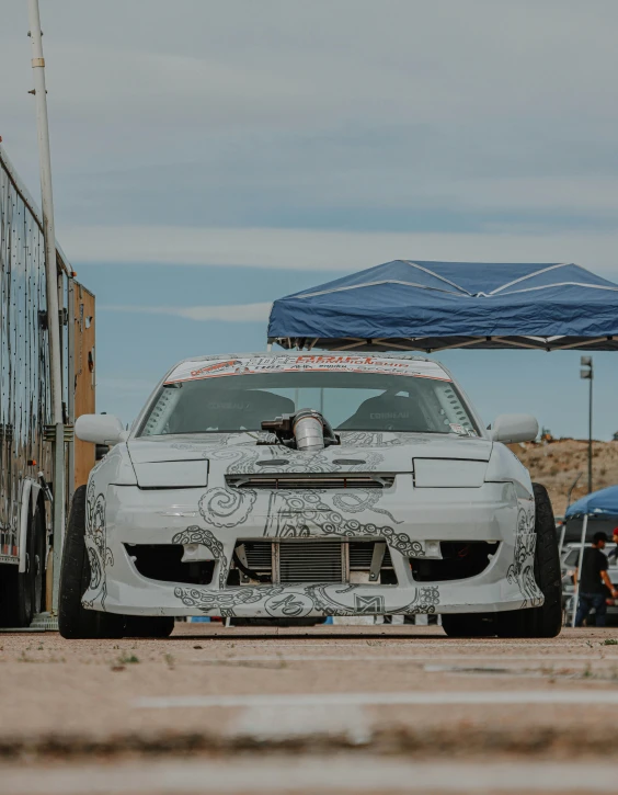 an old race car with graffiti covered hood sits by a trailer