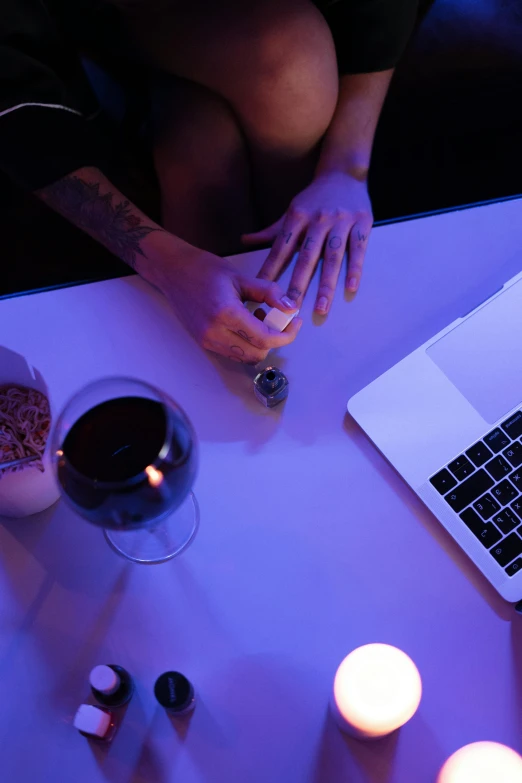 a table with someone's hand on a laptop and a small glass of wine