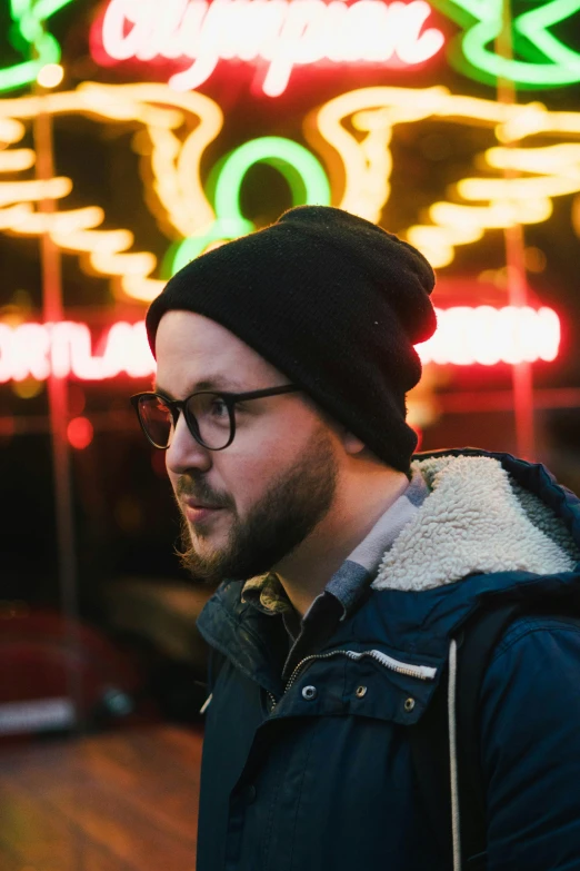 man with glasses in front of a neon sign