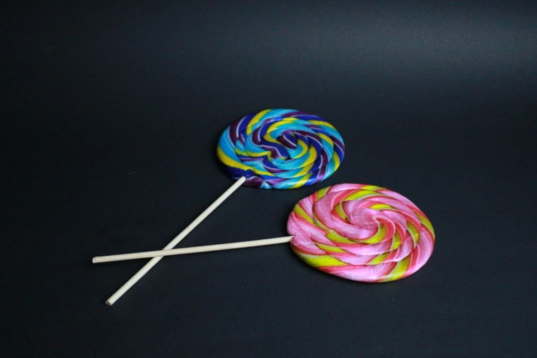 two colorful lollipops are on a black surface