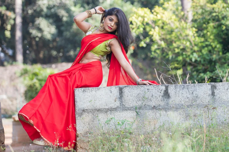 an indian woman in a red sari poses on a wall