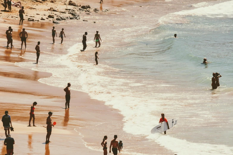 a crowded beach with people carrying surfboards and onlookers