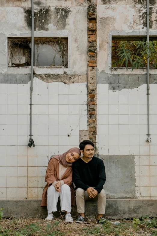 a couple is sitting by a wall on a phone