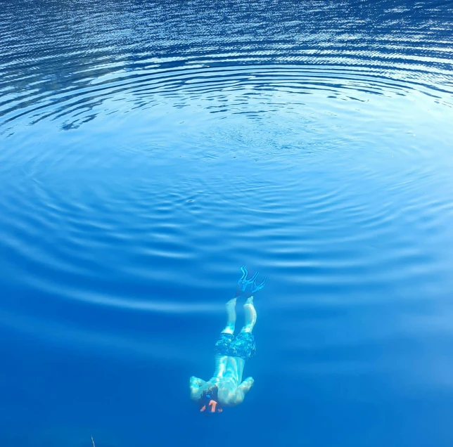 a man swims in the water as a blue sky is reflected